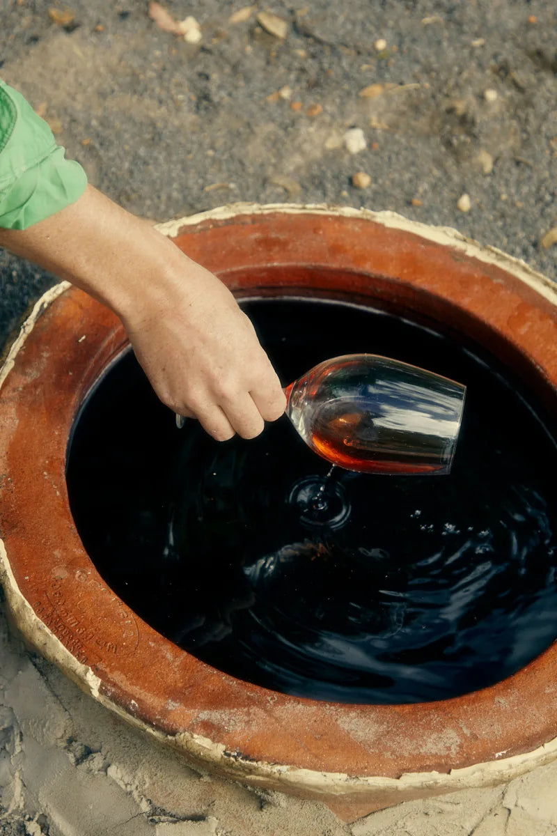 A hand sampling wine from a clay qvevri