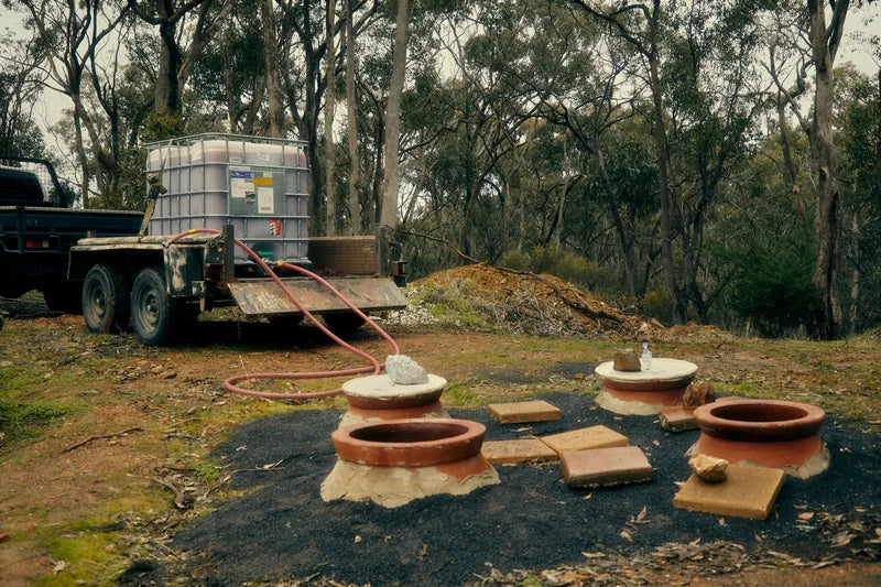 Clay qvevri set into the ground beside a work truck and trees